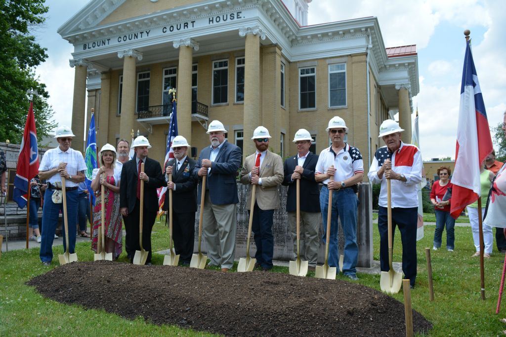 Eight shovelers with hardhats on, with shovels, in front of patch of dirt