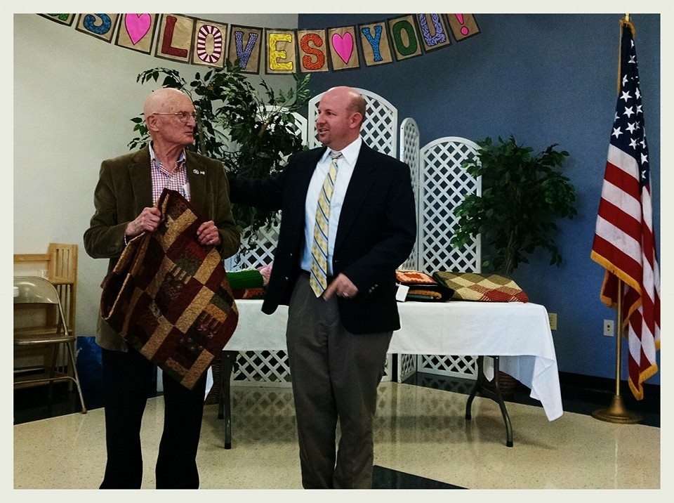 Man gifting a veteran a brown and red quilt