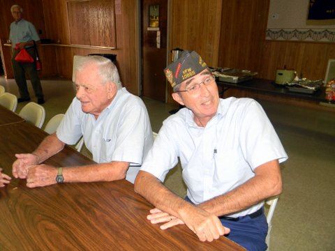 Two men in conversation, sitting at a table one with a hat on