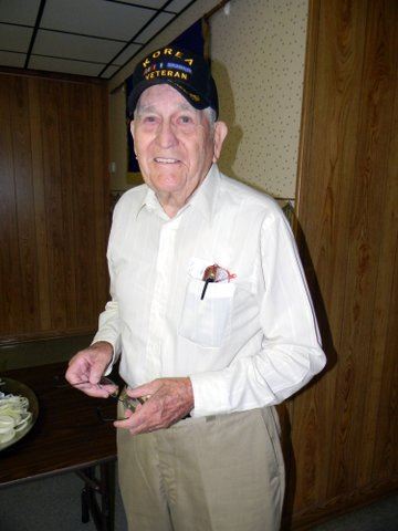 Man in white oxford with Korean war veteran hat on, standing and smiling