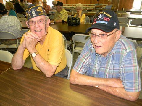 Man in yellow shirt besdie man in blue plaid shirt, sitting at a table talking