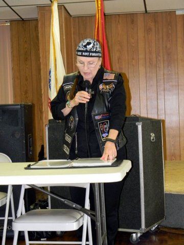Woman standing at table with microphone, reading from binder