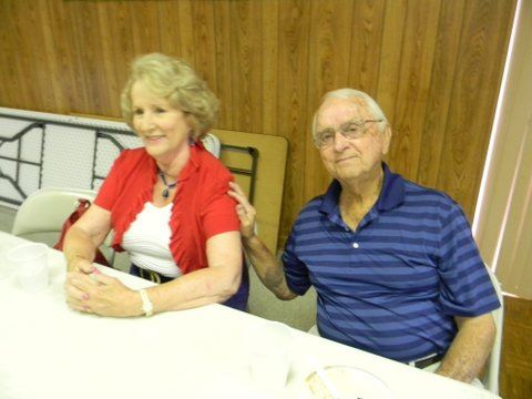 Woman in red and white sitting beside man in blue, man has arm on woman's shoulder
