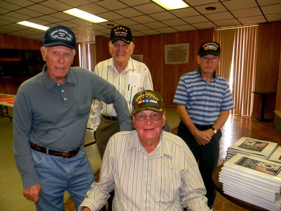 Groups of four veterans, one sitting the others standing, all wearing Korean War veteran hats and smiling