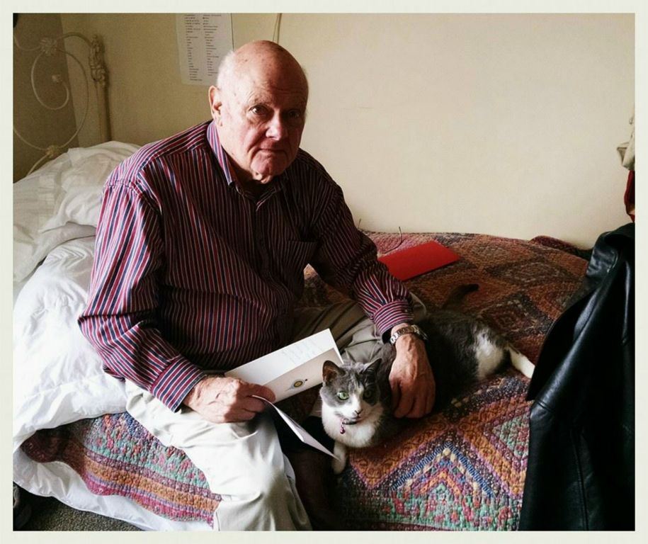 Veteran sits on bed with cat, and card in hand