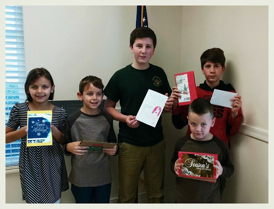 Five children, one girl and four boys, hold up cards, standing in front of American flag