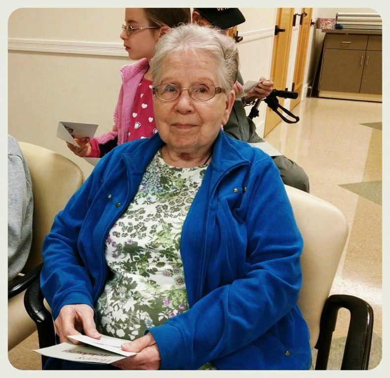 Sittign woman in blue with glasses has card in hands, looking into camera