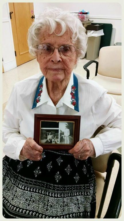 Woman in white shirt looks into camera and holds black and white photographs of soldier