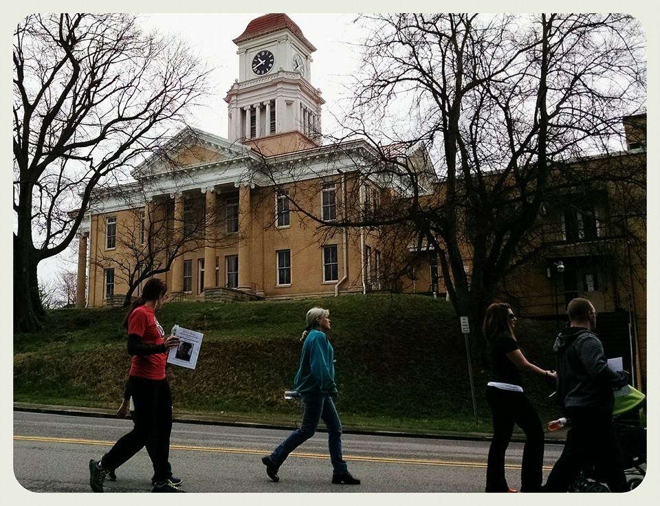 Groups walks down street, in front of building with tower