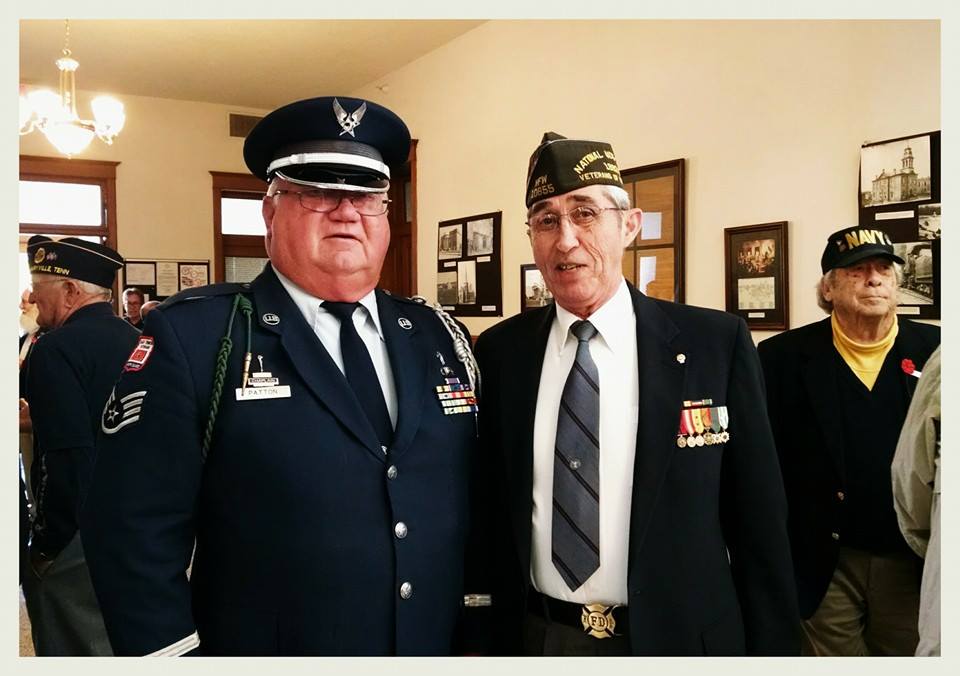 Man in AirForce dress uniform stands with man in black suit with medals on lapel