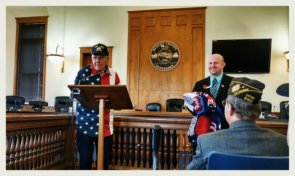 Man wearing Iwo Jima Survivor hat and American flag shirt speaks at wooden podium inside courtoom