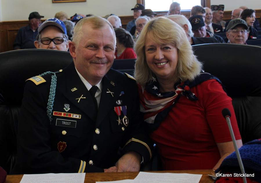 Man in Army decorated dress unifrom smiles with lady in red beside him, both sitting