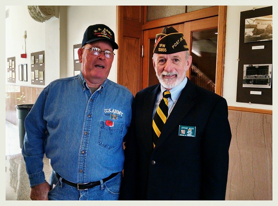 Man in jean shirt and pants with Army hat stands with man in black suit, in hallway of Court house