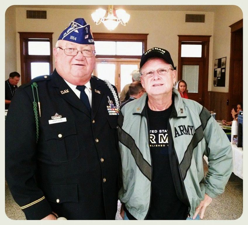 Two veterans, one in dress uniform and one in Army PT jacket stand together inside court house internal room