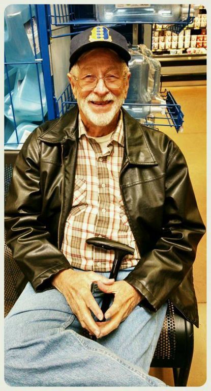 Smiling man with glasses, plaid shirt, and black leather jacket looking into camera while sitting down