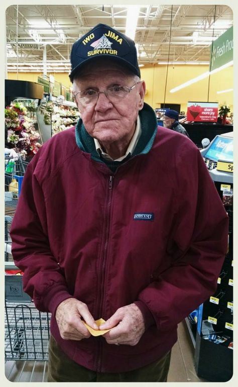 Man in maroon zippered jacket at store, looking into camera, wearing Iwo JIma Survivor hat