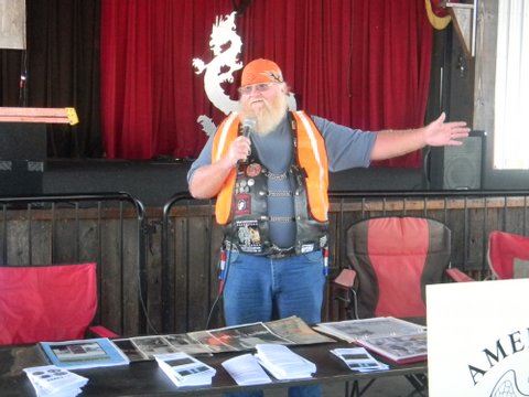 Man in orange vest stands behind table with brochures and pamphlets with microphone
